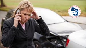 Woman on phone upset in front of a car with front end damage.